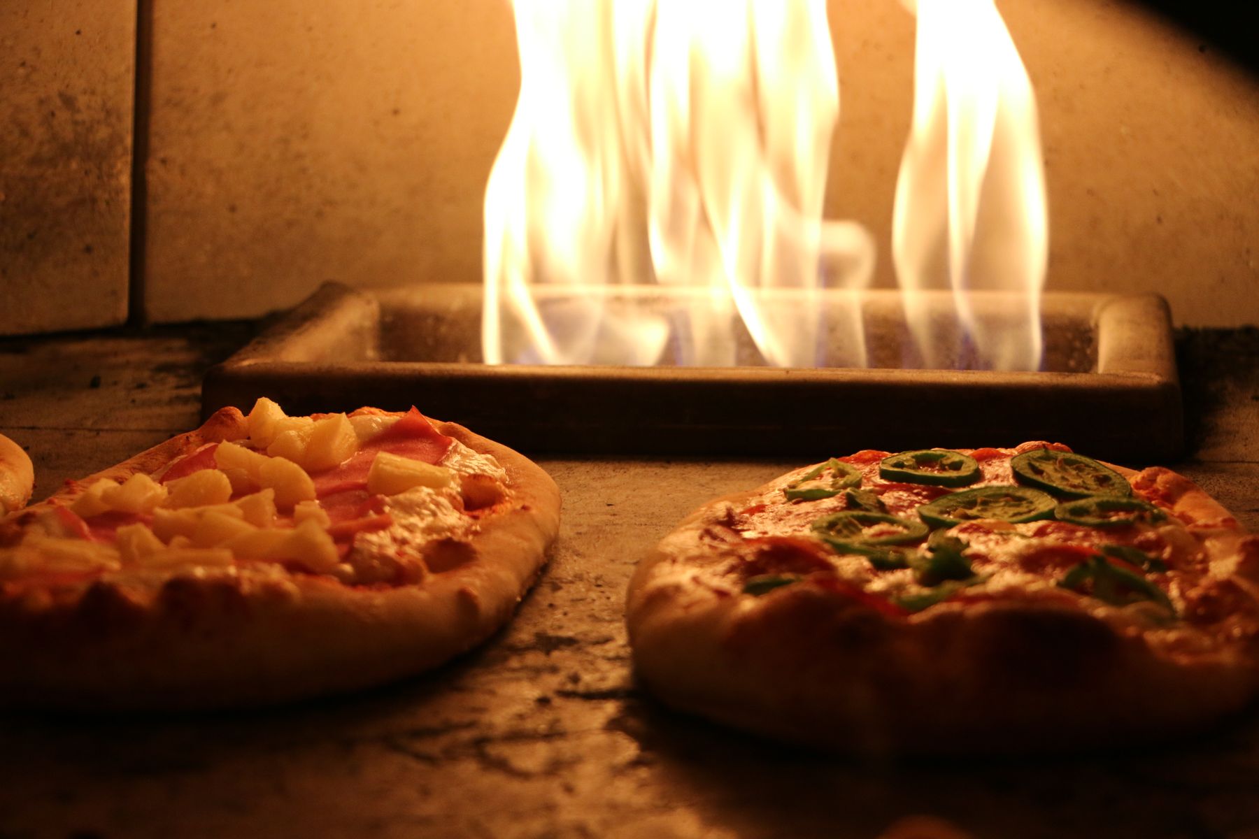 Two pizzas cooking side by side in the wood-fired oven