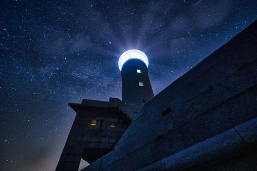 Free A stunning lighthouse silhouetted against a starry night sky, featuring a dramatic low-angle shot. Stock Photo