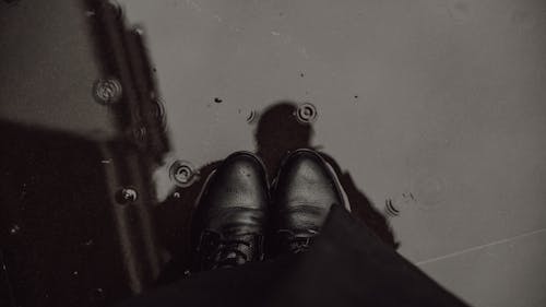 A Person Wearing Black Leather Shoes Standing on Water Puddle
