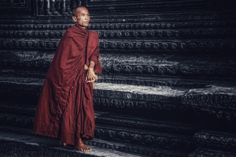 A Buddhist monk in a red robe at ancient temple steps