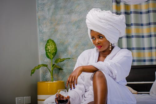 Woman in White Bathrobe Sitting while Holding a Glass of Wine