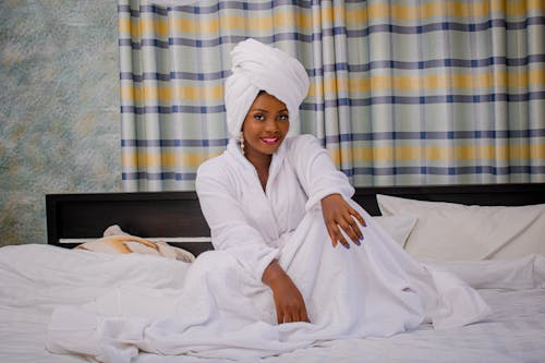 Free Woman in White Bathrobe Smiling while Sitting on Bed Stock Photo