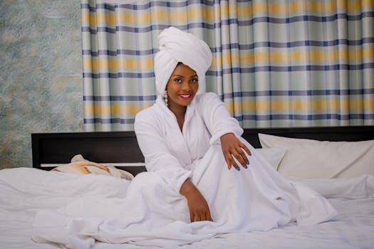 Smiling woman in bathrobe sitting on a bed in a hotel room, embodying relaxation and leisure.