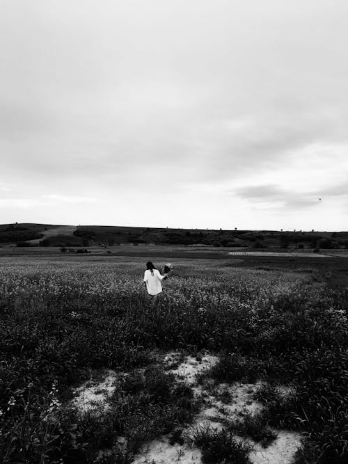 Grayscale Photo of Woman in White Dress Standing on Grass Field