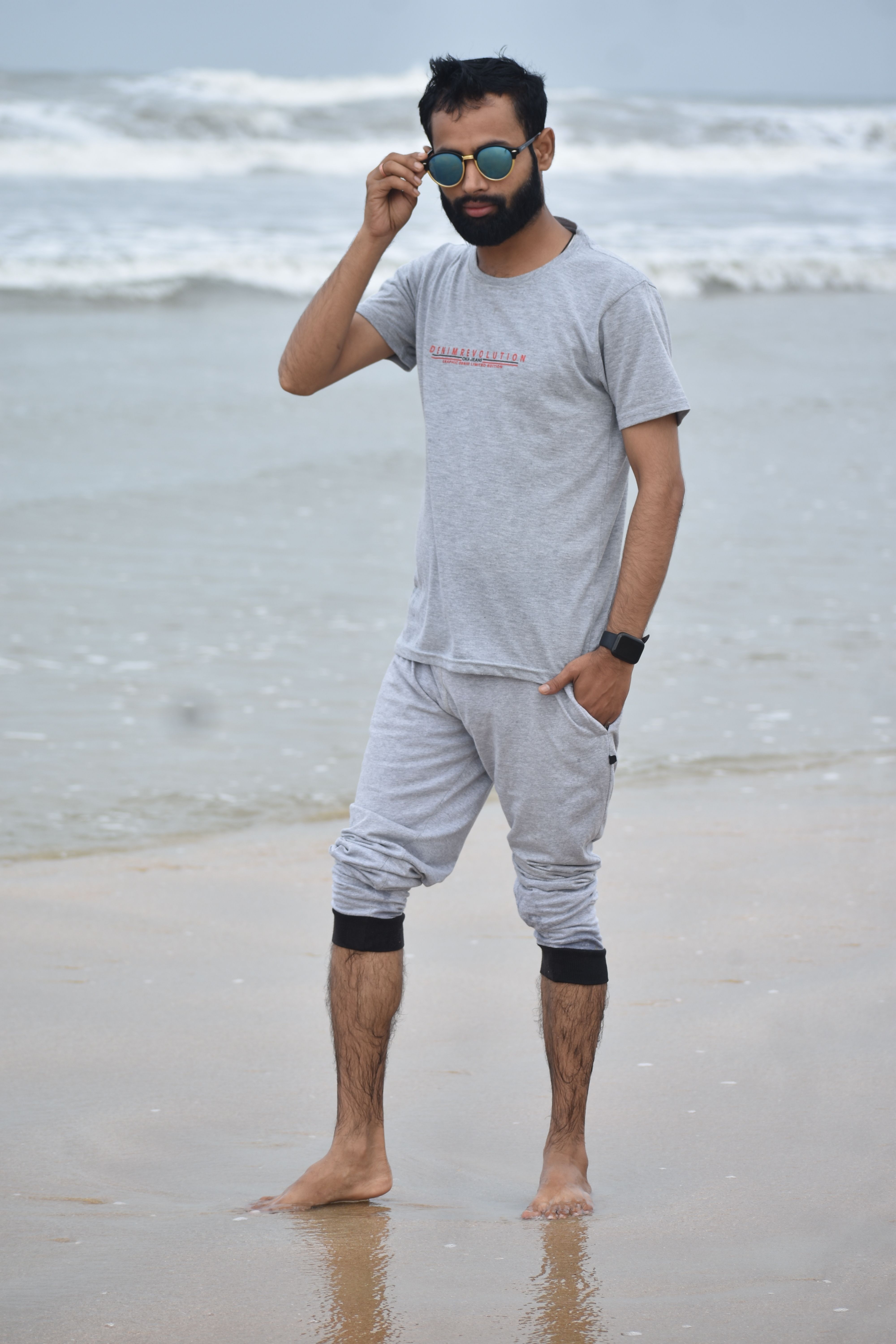 Barefoot man in casual wear and sunglasses posing on a serene beach shore.
