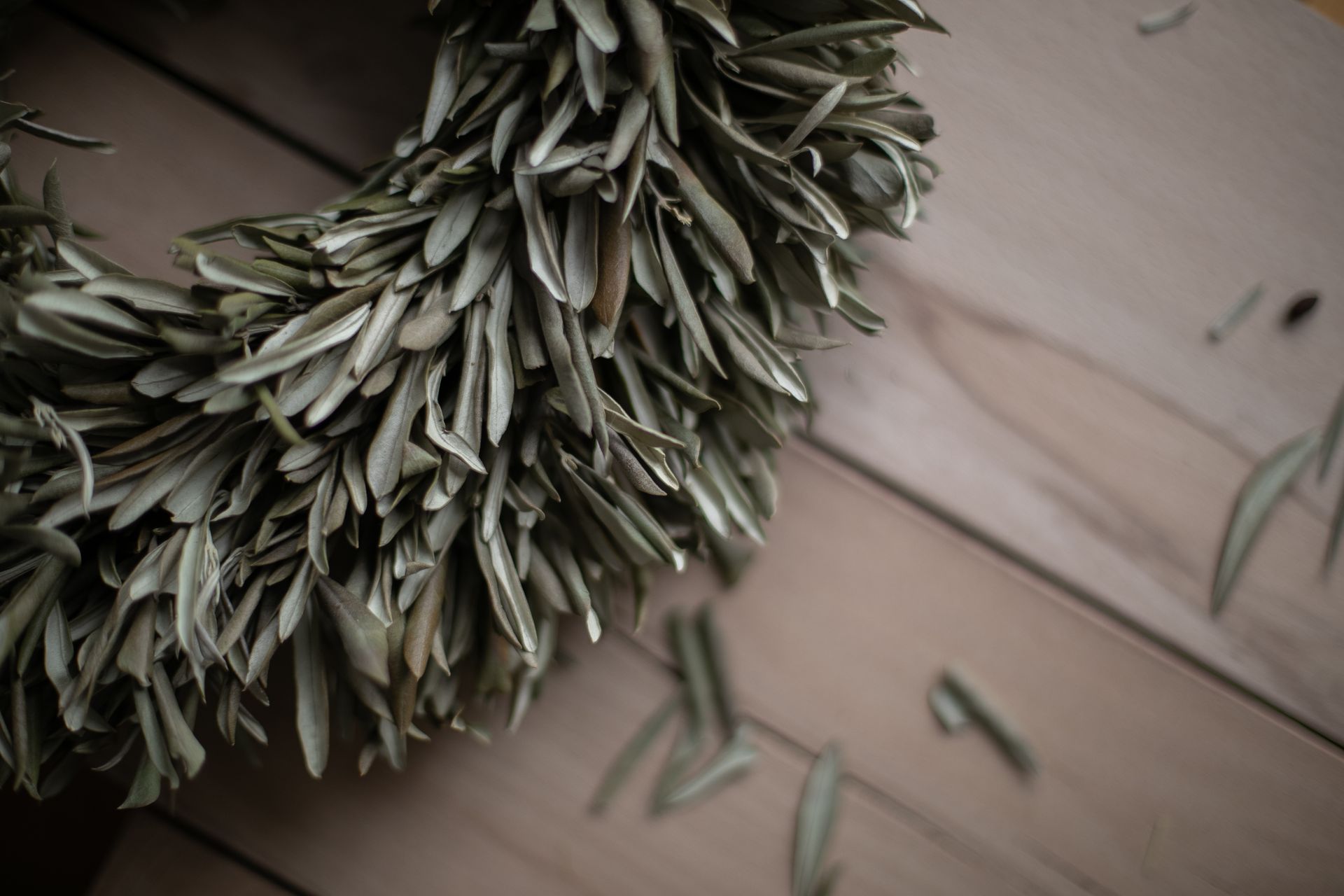 Close-up of a dried olive leaf wreath on a wooden table, conveying rustic charm.