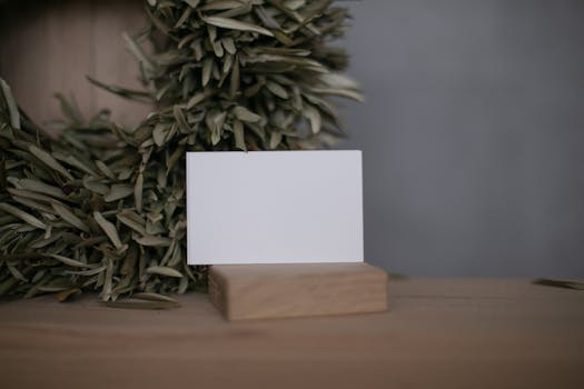 A minimalist business card on a wooden stand surrounded by olive leaves, offering ample copy space.