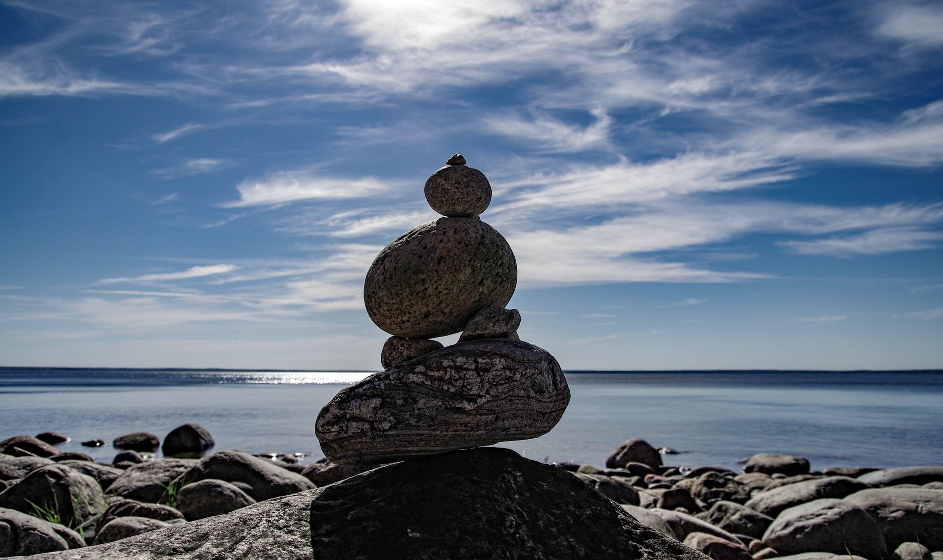A tranquil scene of balanced rocks by the ocean under a clear blue sky.