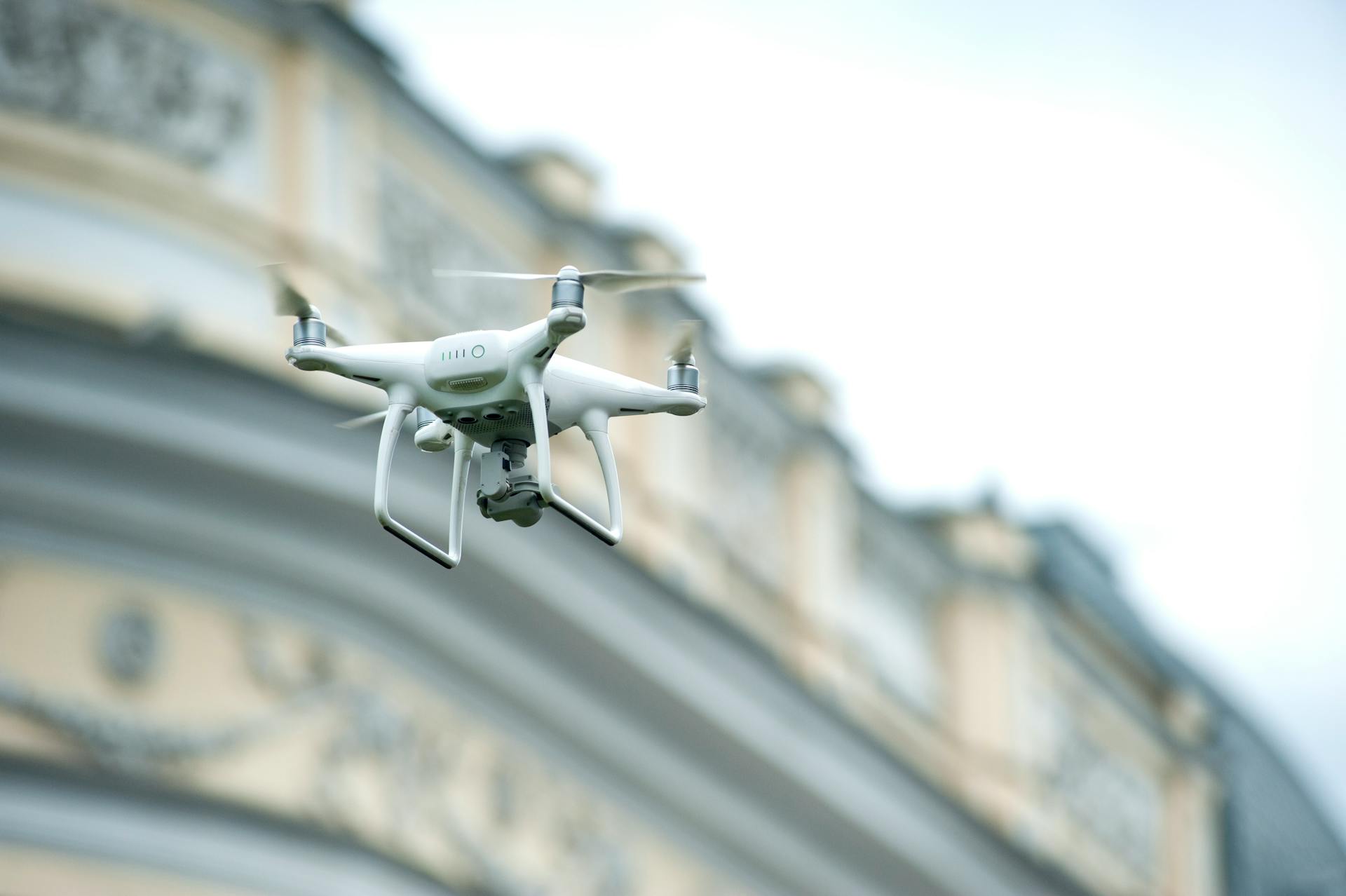 Quadcopter drone hovering near a classic building in bright daylight.