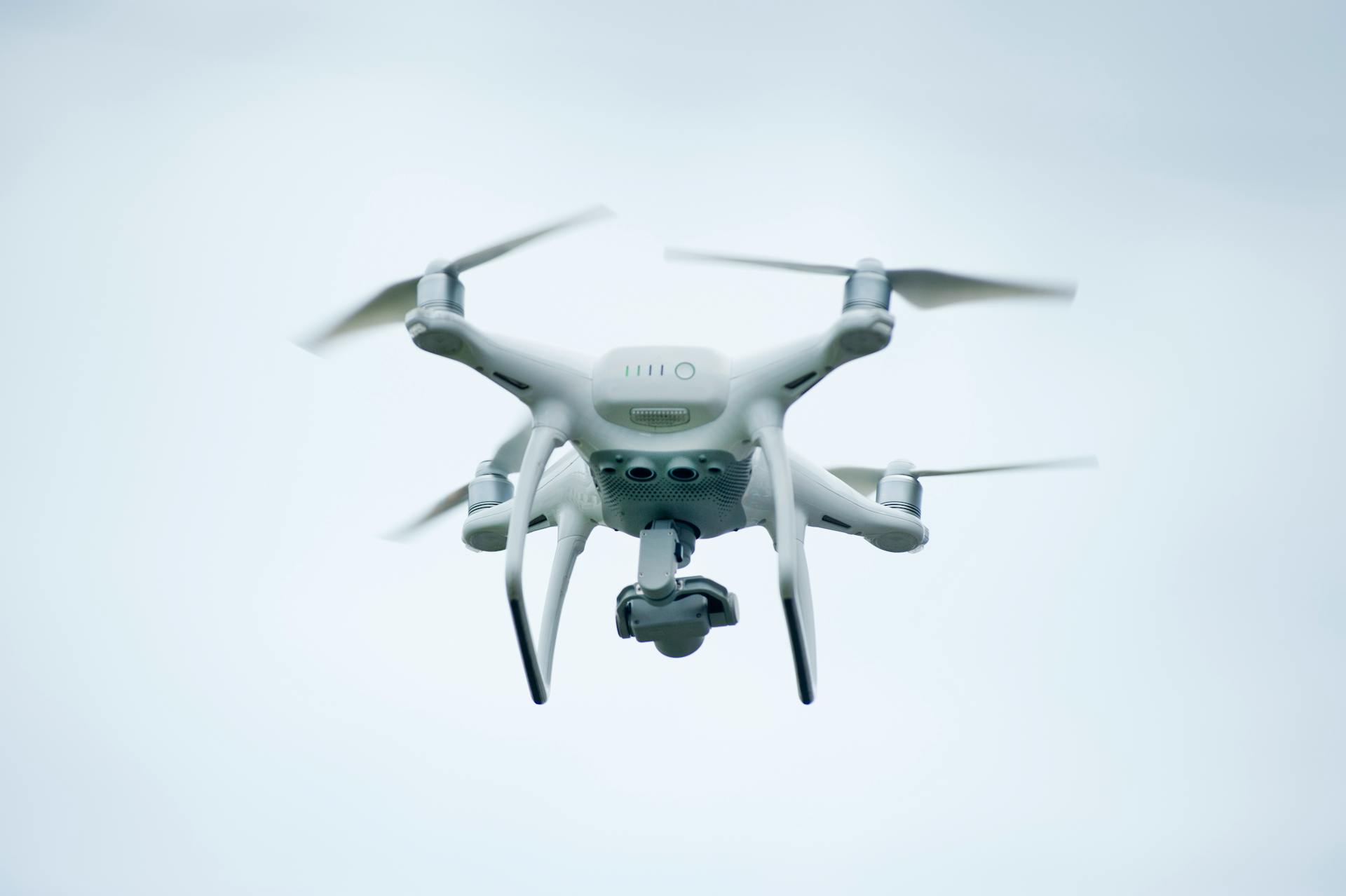 A white quadcopter drone captured flying against a clear sky, showcasing modern technology.