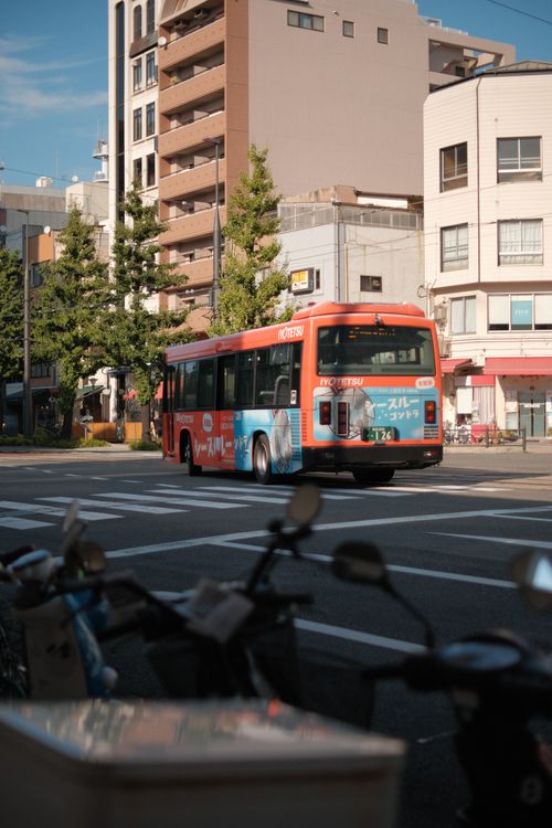 Free Colorful public bus driving through a bustling city street with buildings and bicycles. Stock Photo