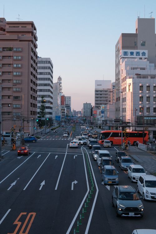 Free Busy city street with traffic and buildings in evening light, showcasing urban life. Stock Photo