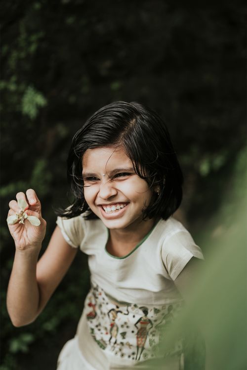 Free Smiling young girl with a flower in hand, enjoying nature. Captures the essence of childhood joy. Stock Photo