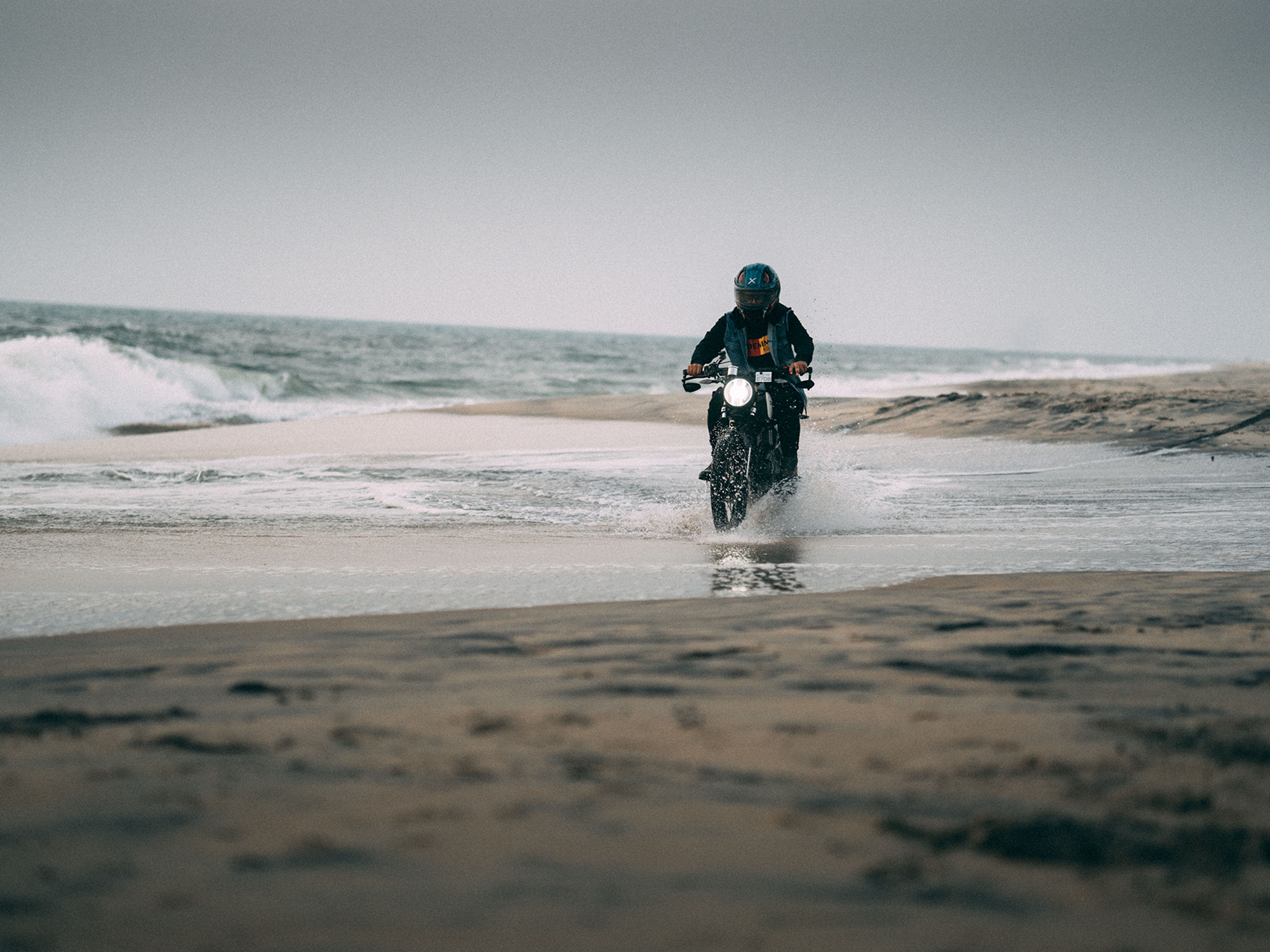 Rider on a motorcycle navigating shallow waves along a sandy beach.