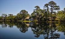 在晴朗的天空下，美丽的湖边家园周围的树木倒映在平静的水面上