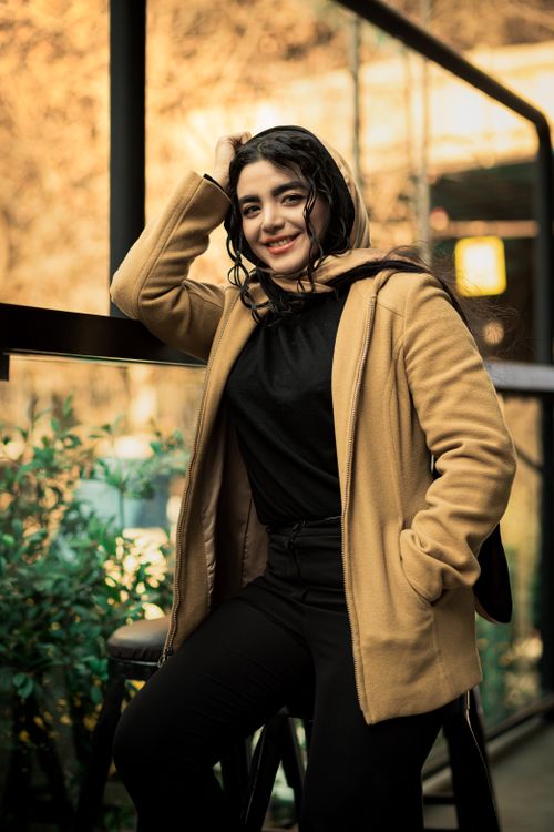 Free A cheerful woman in a brown coat poses outside against a glass wall, exuding warmth and style. Stock Photo