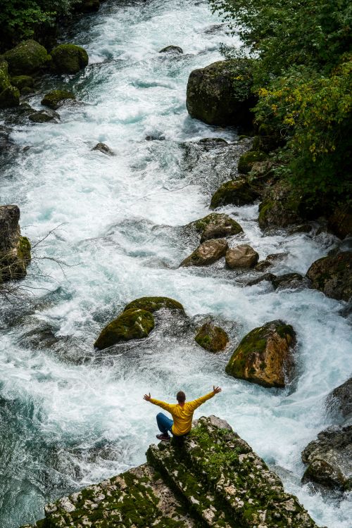Free A person celebrates nature sitting at a cliff's edge over a flowing river. Stock Photo