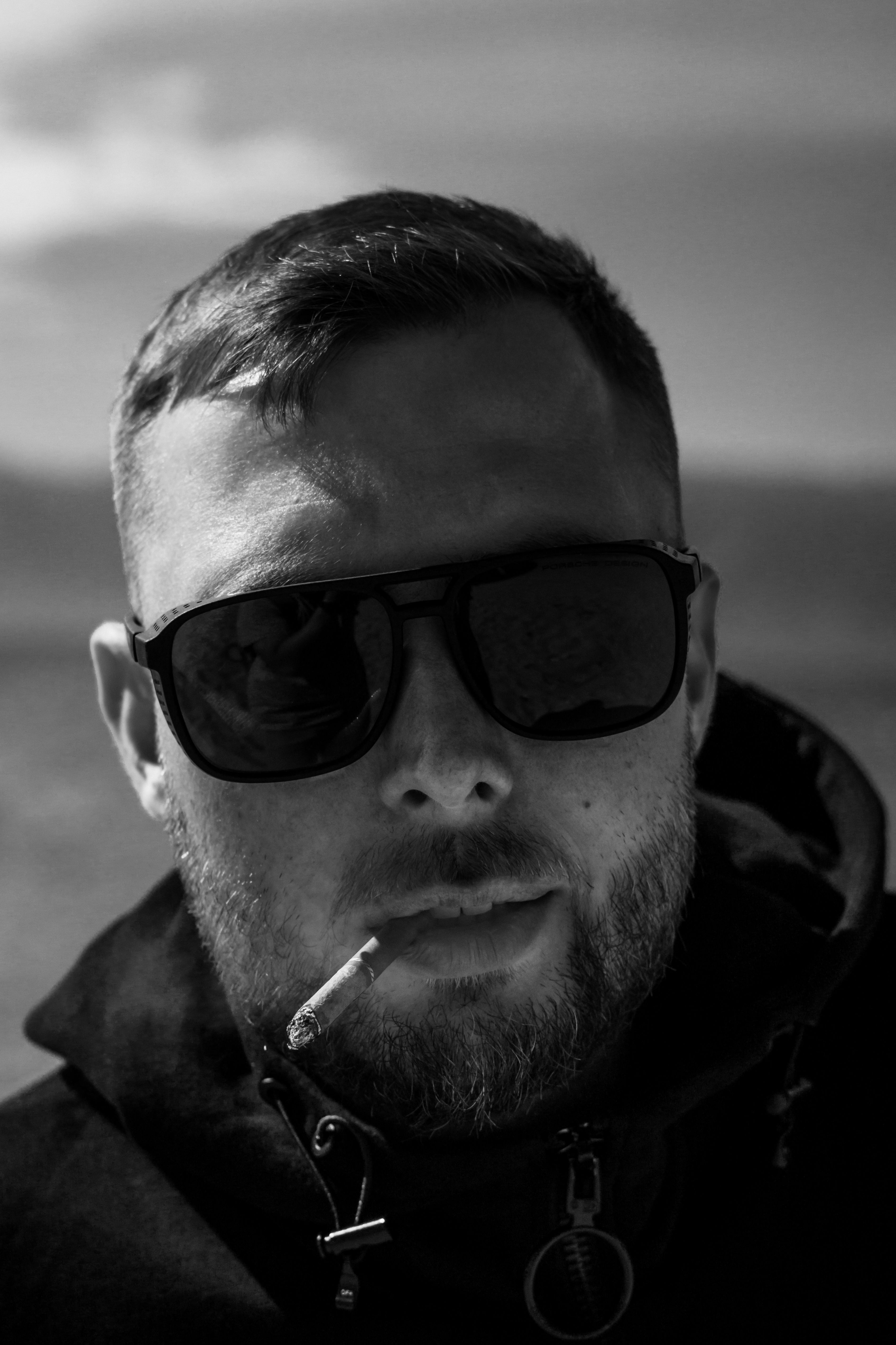 Black and white portrait of a man with sunglasses smoking outdoors.