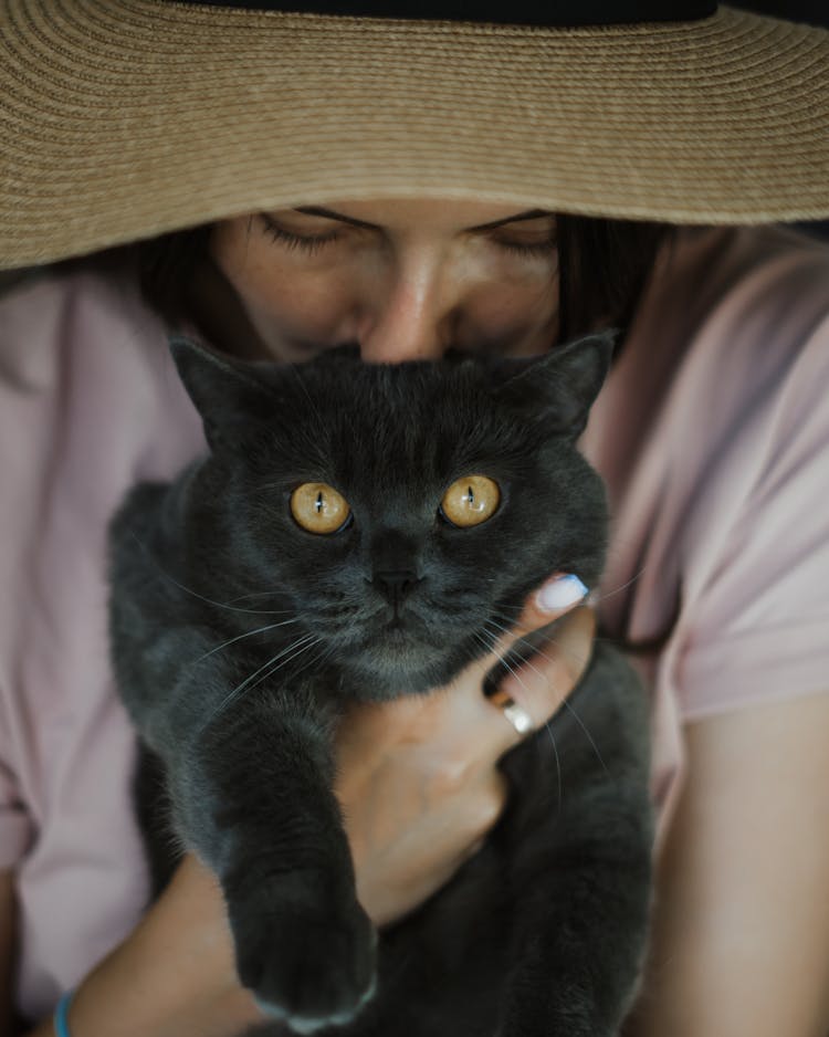 A Woman With A Brown Hat Kissing A Black Cat 