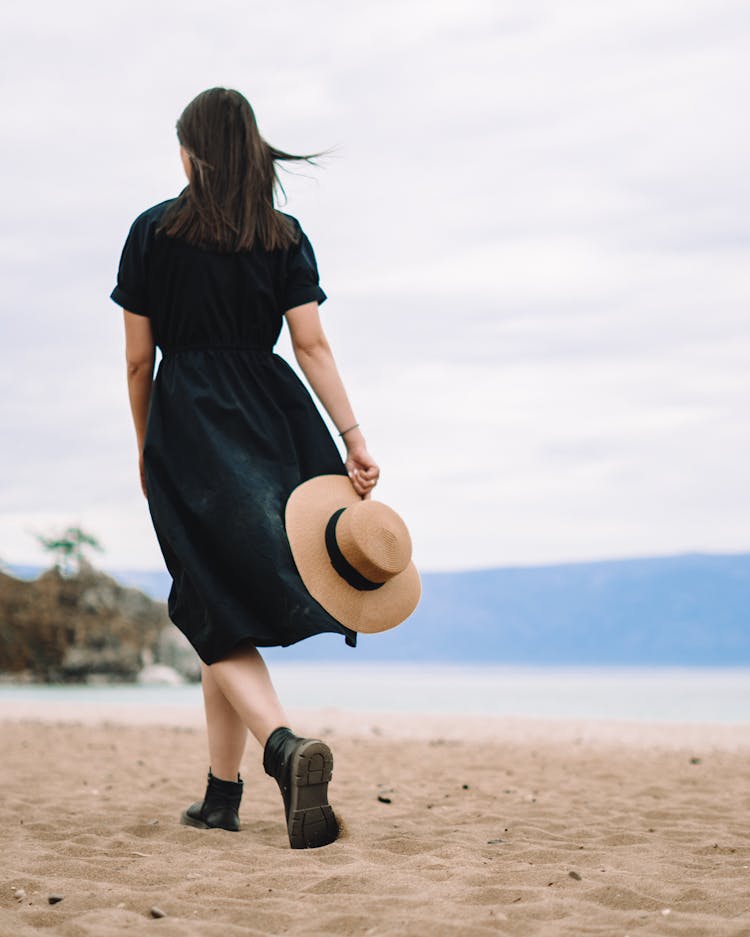 Woman In Black Dress Walking On A Beach 