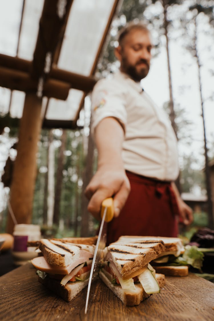 A Man Slicing A Sandwich On A Wooden Table