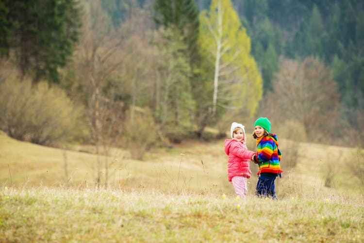 Two Little Girls Playing In Meadow With Forest In Background