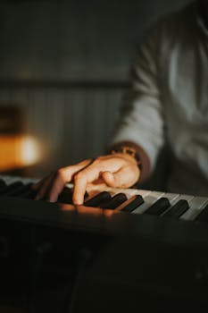 A man playing a keyboard with focus on his hands and wristwatch, in warm lighting.