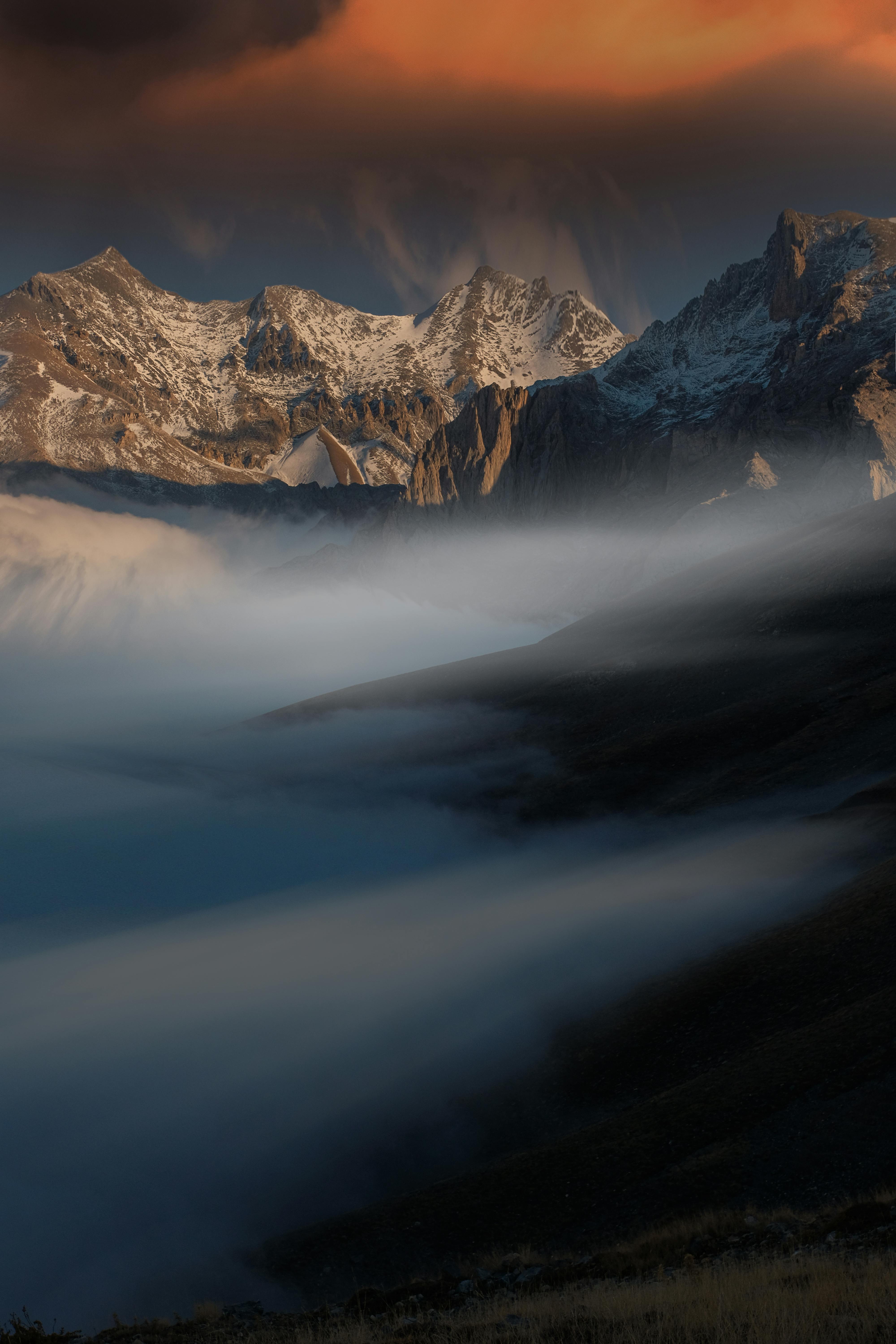 Serene view of misty mountains at sunset with snow and dramatic skies.