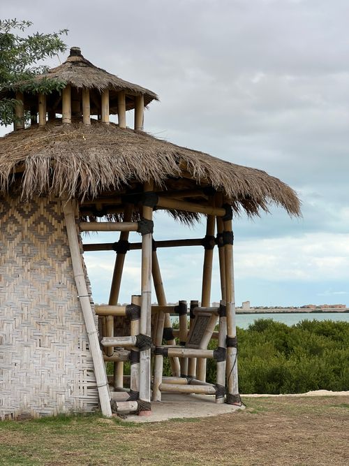 Free Beautiful rustic gazebo with thatched roof by the waterfront under cloudy sky. Stock Photo