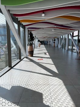 Bright and spacious airport corridor featuring a colorful, modern ceiling design and large windows.