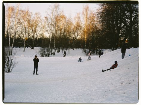 People enjoying winter activities in a snow-covered Moscow park, surrounded by bare trees.