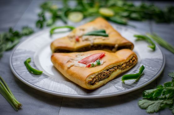Two golden bread parcels filled with spiced minced meat, topped with tomato and green chili