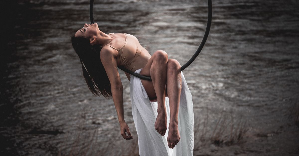Woman on aerial hoop artfully poses by the water, embracing grace and strength.