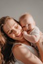 A joyful mother lovingly hugs her smiling baby, both glowing in warm sunlight.