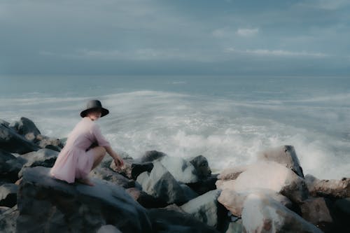A Woman in Pink Dress and Black Hot on Rocky Shore