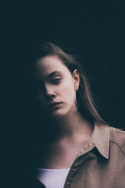 Free A dramatic close-up portrait of a young woman with a moody expression against a dark background. Stock Photo