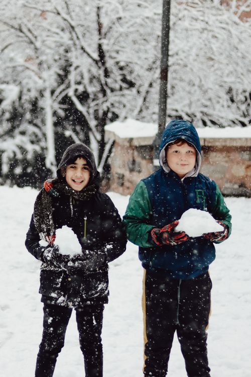 Free Two boys playing with snowballs amidst a picturesque snowy winter scene, capturing playful joy. Stock Photo