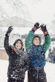 Two boys cheerfully playing in the snow during a snowy winter day, having fun outdoors.