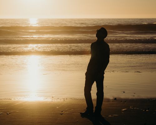 Free Silhouette of a person standing on a serene beach during sunset, reflecting tranquility. Stock Photo