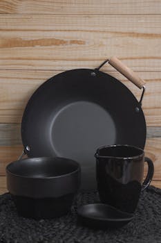Sleek black ceramic bowl, jug, and pan on rustic wooden background.