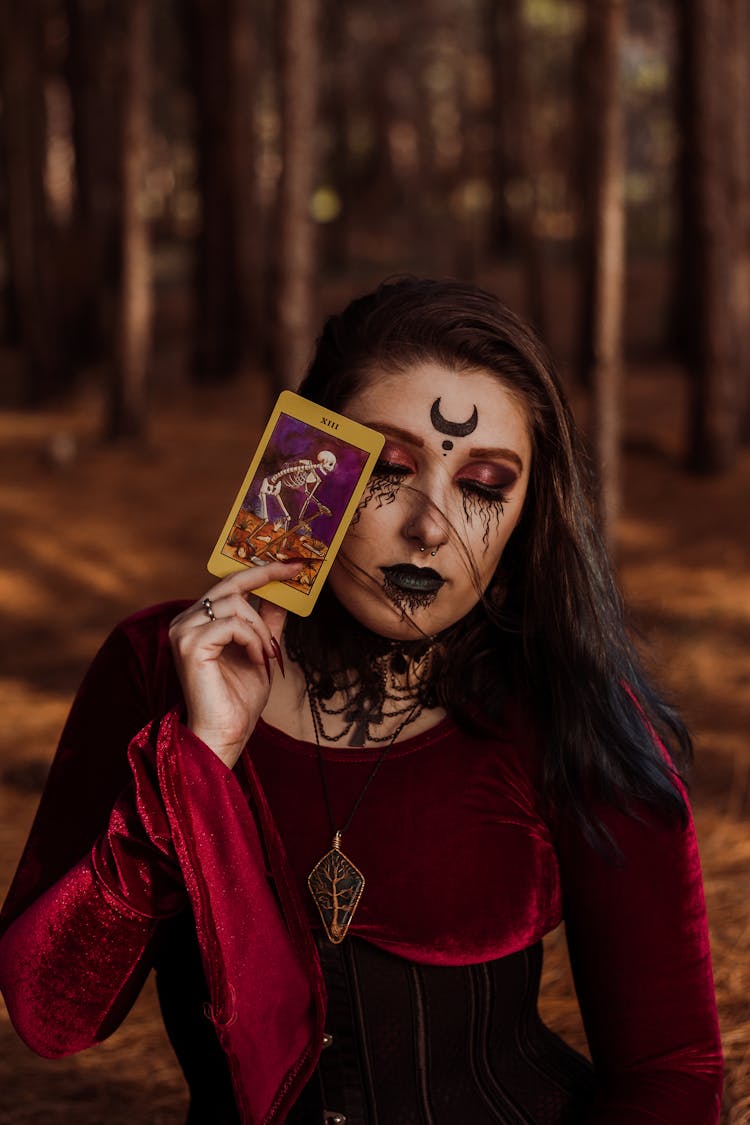 Woman In A Red Dress Wearing Creative Makeup Holding A Tarot Card