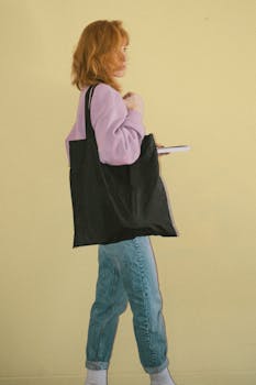 Woman in pink sweater with a tote bag and book against a yellow background.
