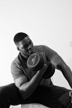 A muscular man lifting a dumbbell indoors, showcasing strength and focus in a black and white setting.