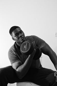 Black and white photo of a muscular man lifting a dumbbell indoors, showcasing strength and fitness.