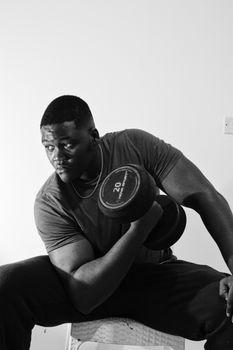 A monochrome image of a man lifting a 20kg dumbbell, captured in a sitting position.