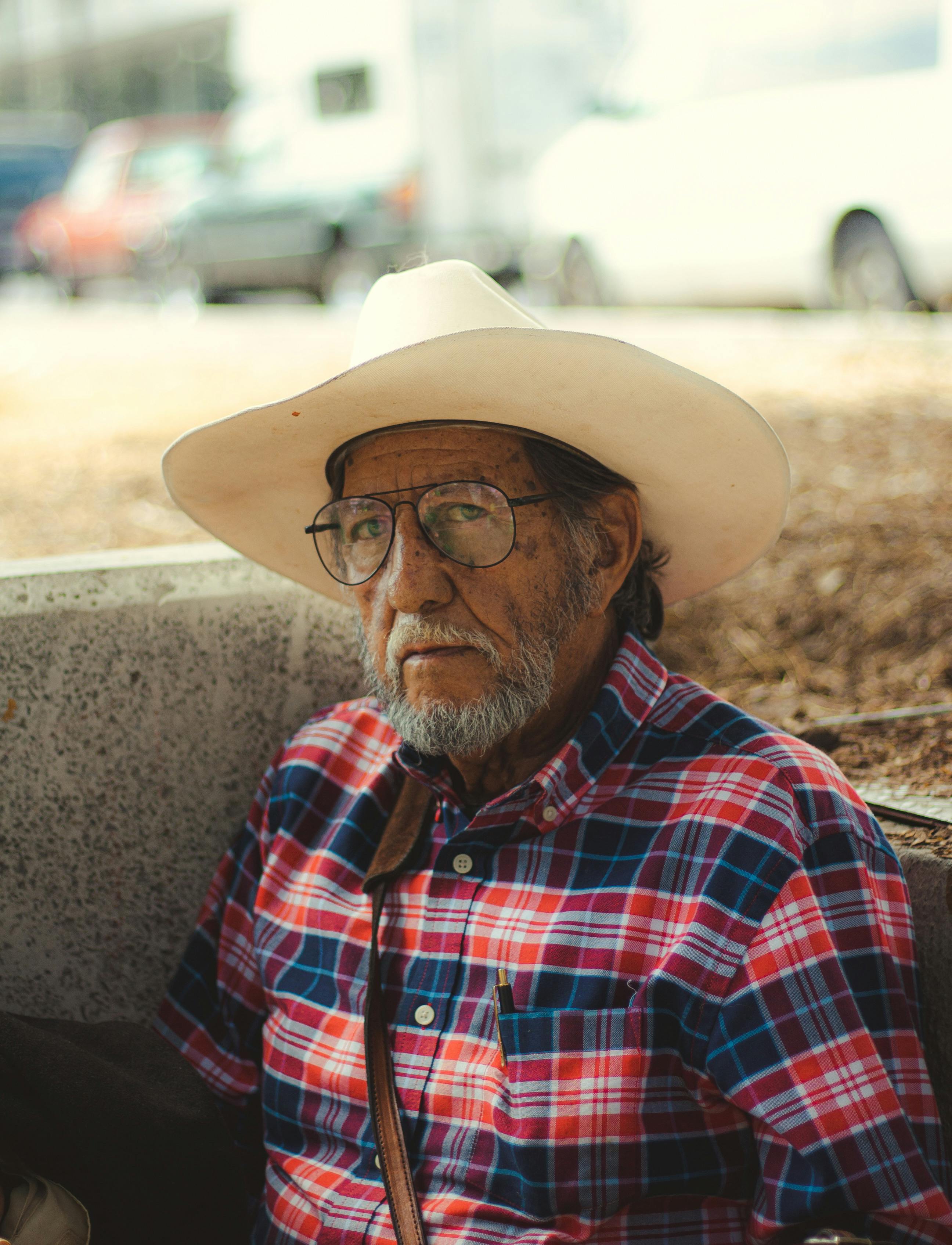 Portrait of a senior man sitting outdoors wearing a checkered shirt and cowboy hat.