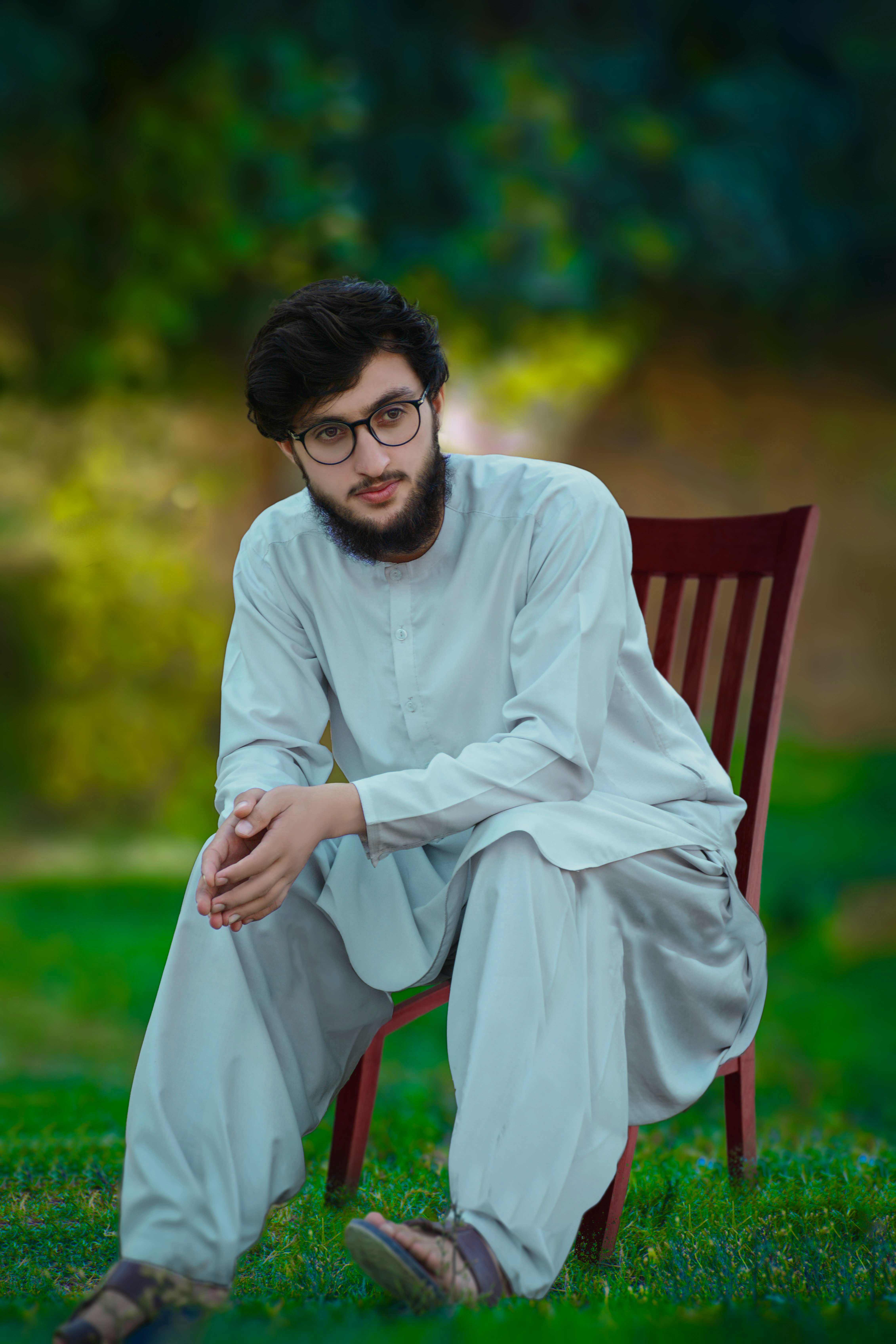 Young man in traditional white shalwar kameez sitting outdoors on a chair.