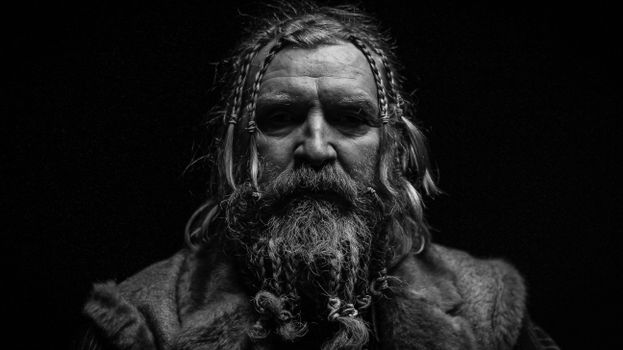 Striking grayscale portrait of a senior man with braided hair and beard against a black background.
