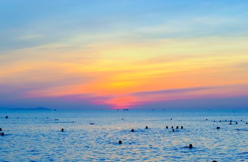 Free Colorful sunset over a tropical ocean with silhouettes of people swimming, creating a serene beach scene. Stock Photo