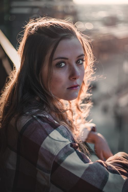 Free A young woman gazes into the distance, illuminated by warm sunset lighting. Stock Photo